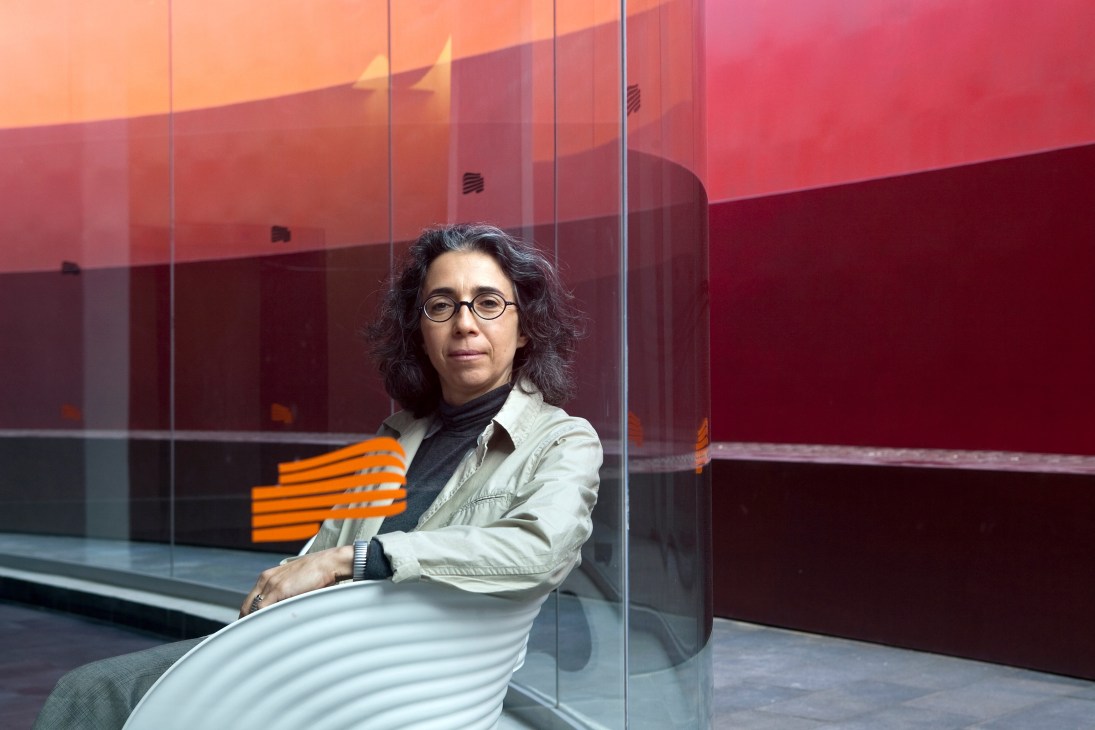 Creative director Galit Gaon seated against crimson glass wall at Design Museum Holon