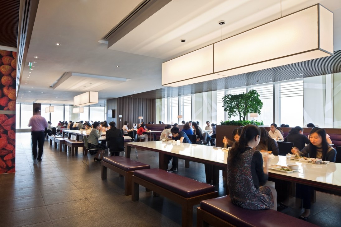 HSBC Shanghai office cafeteria with employees dining at long tables with burgundy bench seating and natural materials throughout.