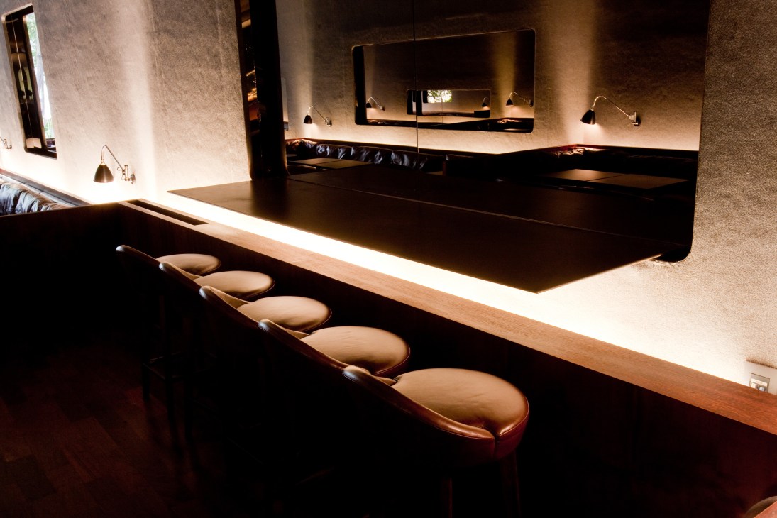 Upholstered bar stools with leather seats line the illuminated counter at Numero nightclub in São Paulo.