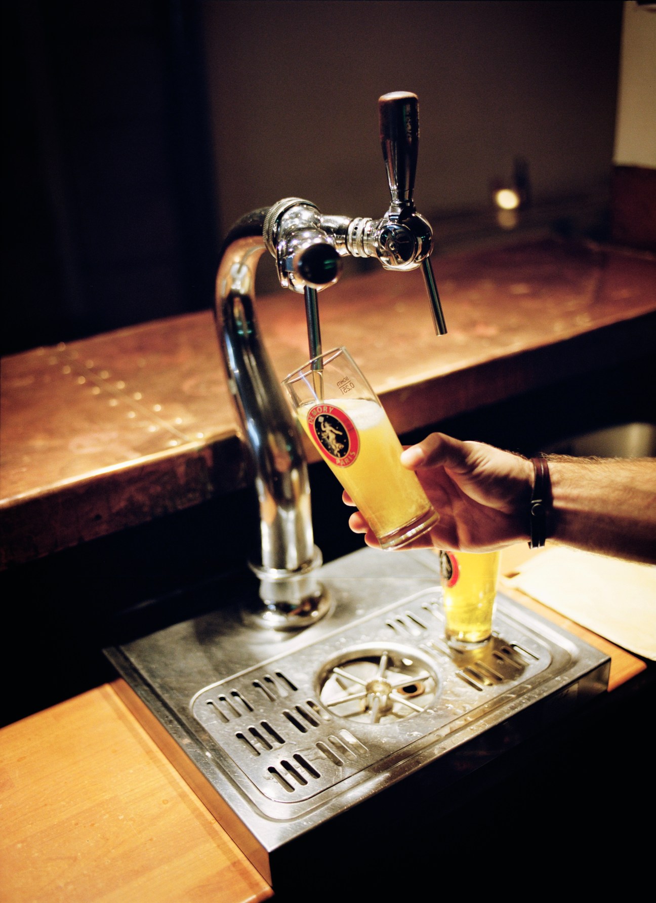 A hand pours golden beer from a tap into a glass at the Demory bar in Paris.