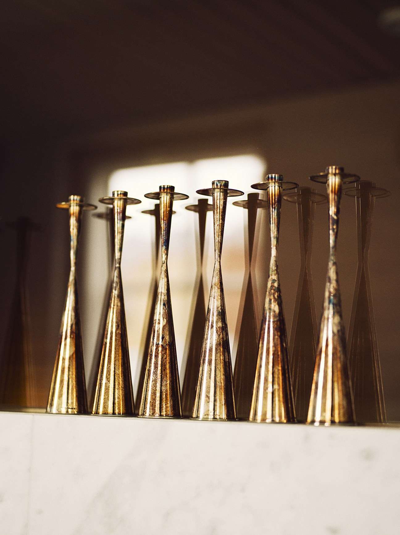 Row of brass TW189 candleholders by Tapio Wirkkala casting shadows in sunlight.
