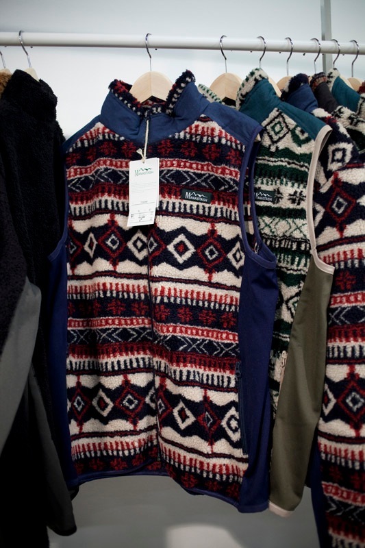 Manastash fleece gilets with geometric patterned designs hung on a rail.