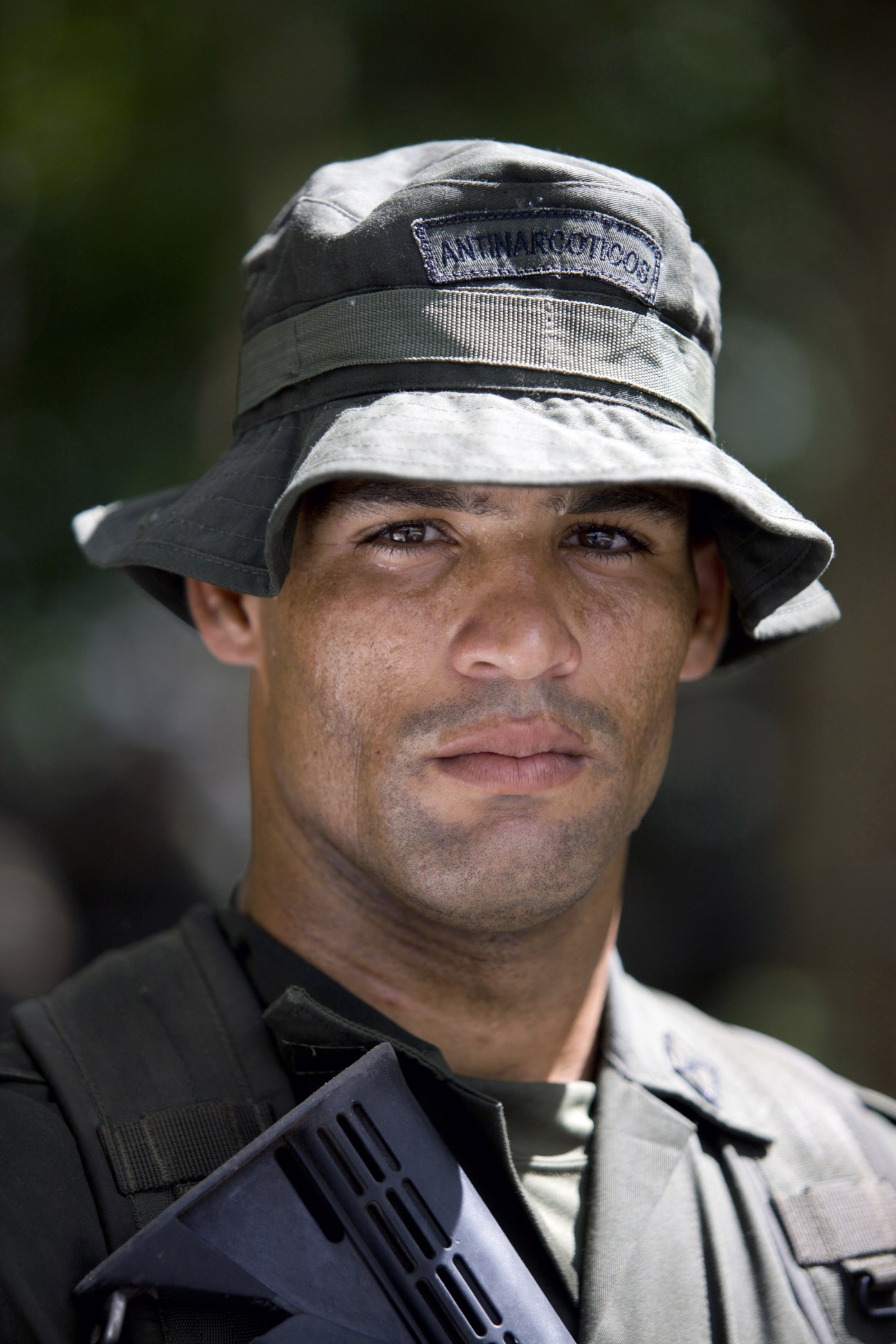 A male police student from the Dominican Republic wearing a bucket hat with anti-narcotics insignia and tactical gear.