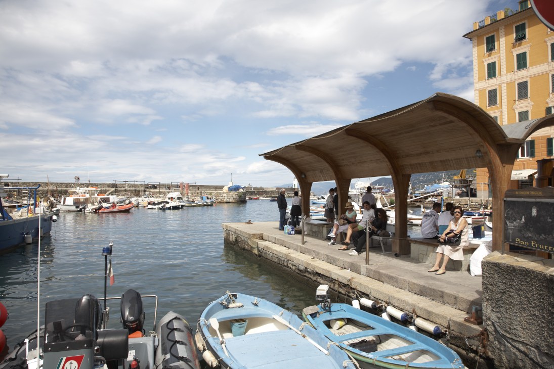 Camogli harbour with moored fishing boats and people waiting under a wooden shelter for water taxis.