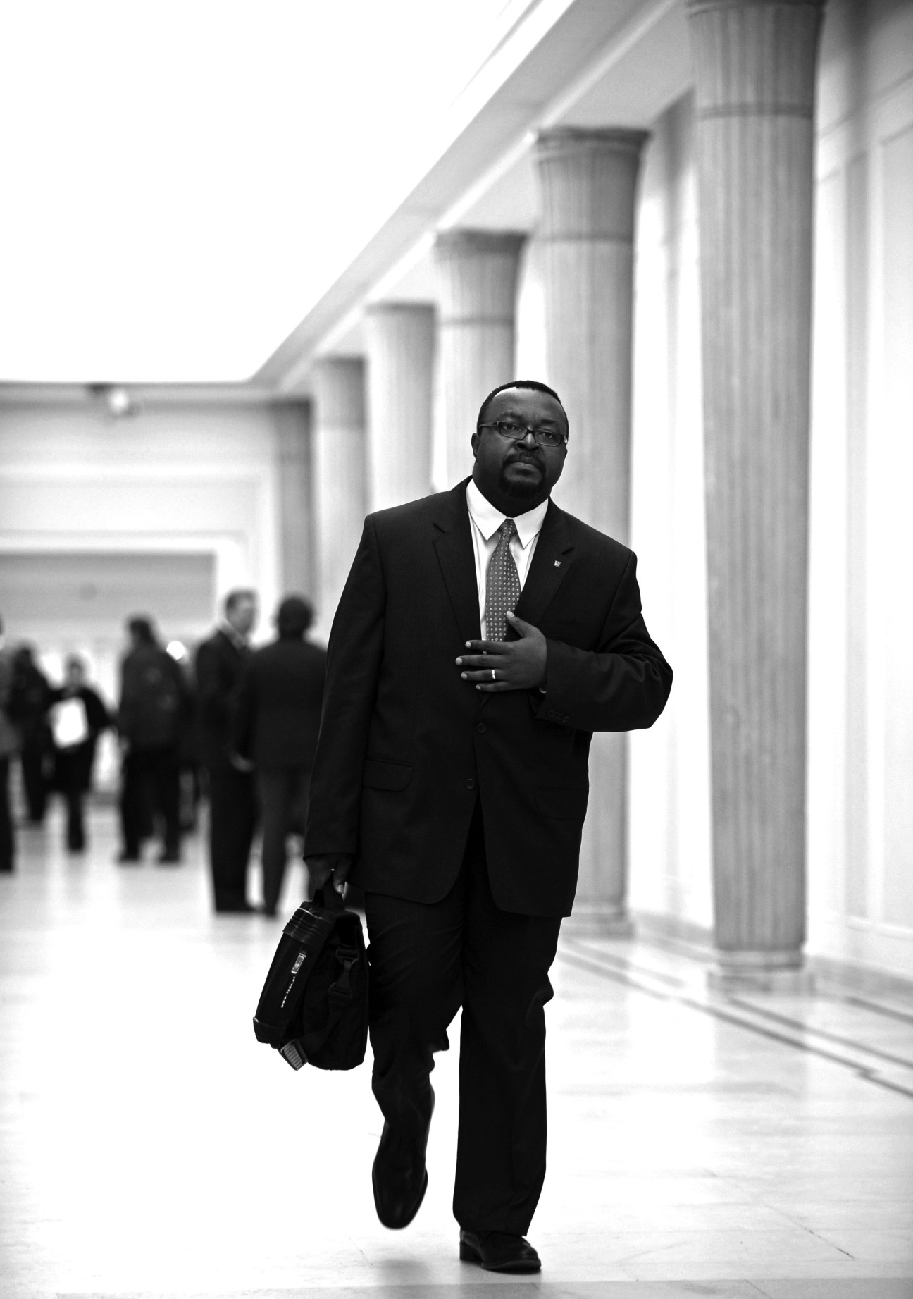 John Godson, Poland's first black MP, walks through a columned parliamentary corridor in formal business attire.