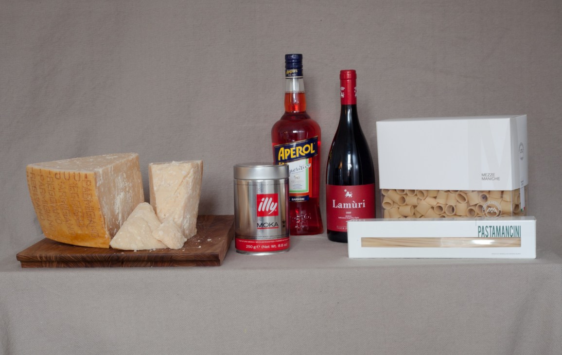 Italian food products including parmigiano-reggiano cheese, Aperol liqueur, Illy coffee, wine and pasta on wooden board.