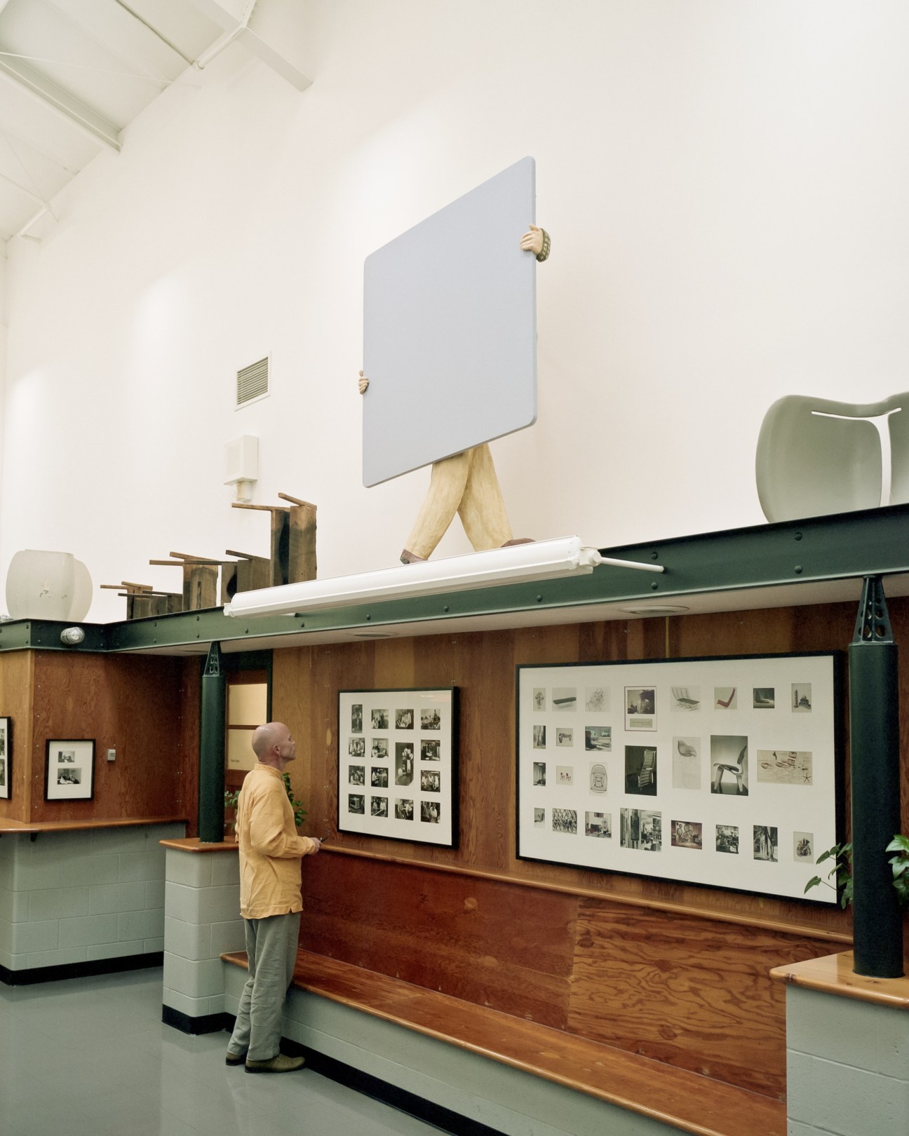 Man viewing framed photographs and design sketches displayed on wooden walls of an archival storage facility.
