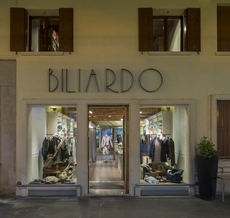 Biliardo multi-brand menswear store storefront in Mirano with illuminated display windows showing clothing.