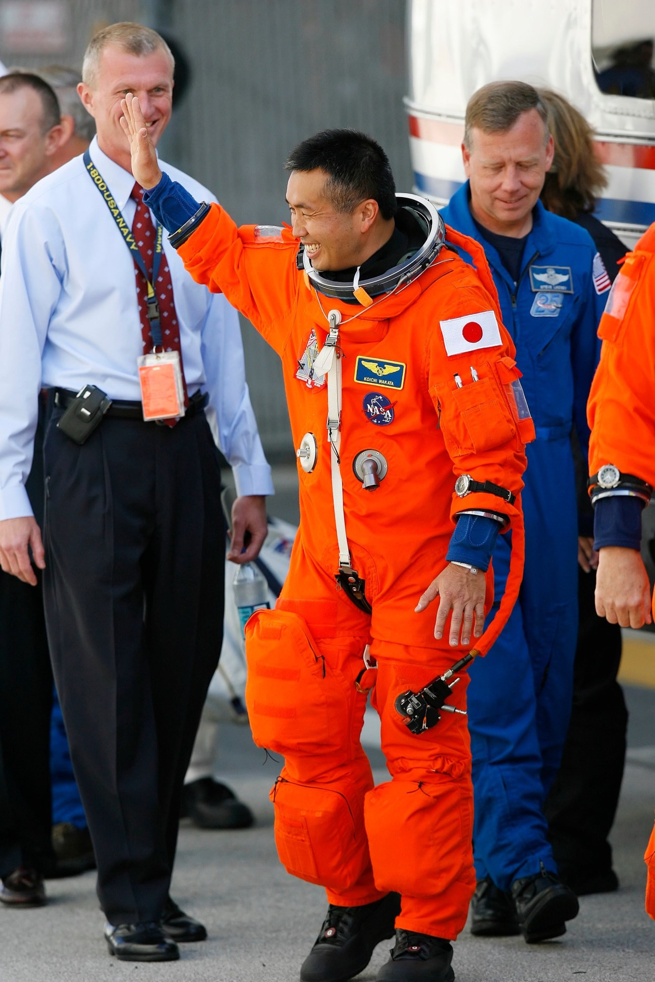 Koichi Wakata in orange spacesuit waving at Kennedy Space Center with NASA officials.