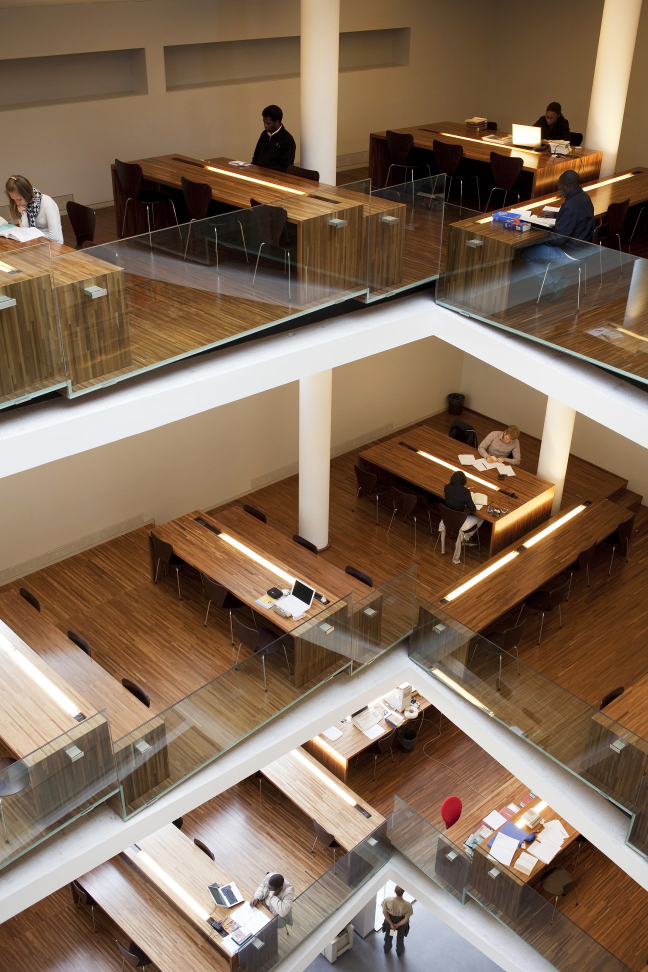 Modern library interior at Pontificia Università Lateranense with multiple wooden floors, white columns, and people studying at desks.