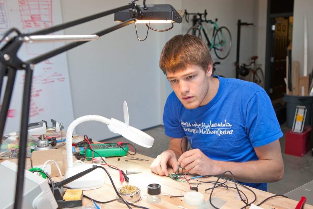 Josh Debner from Deeplocal works on electronics at a workbench in a studio space.