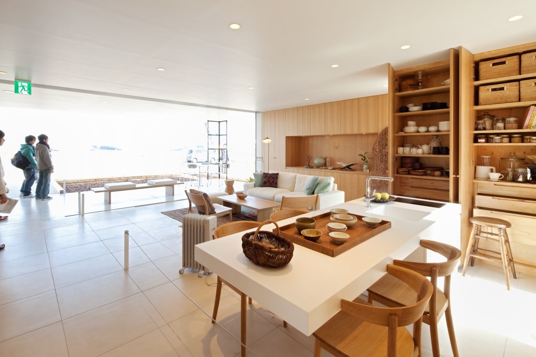 Modern kitchen and living space with wooden shelving, white countertop, and minimalist furnishings by Muji.