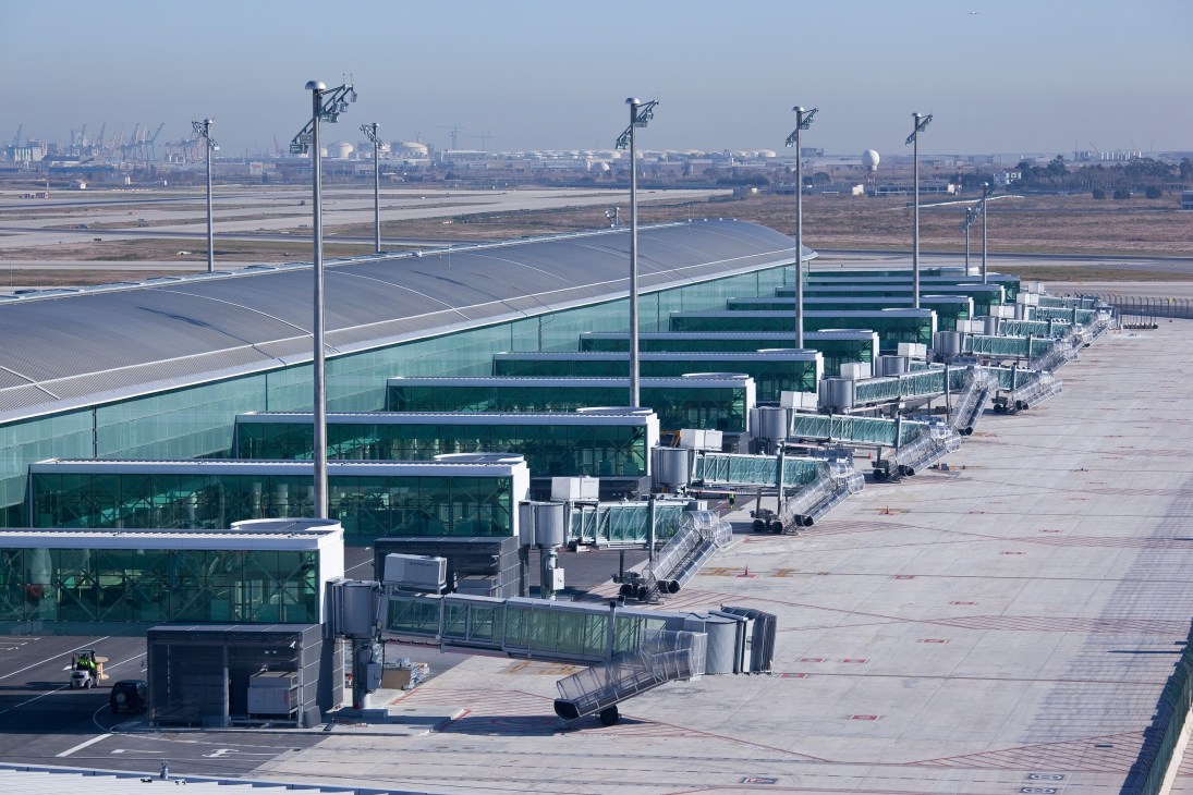Barcelona El Prat airport Terminal 1 with modern gates and aircraft boarding bridges along the tarmac.