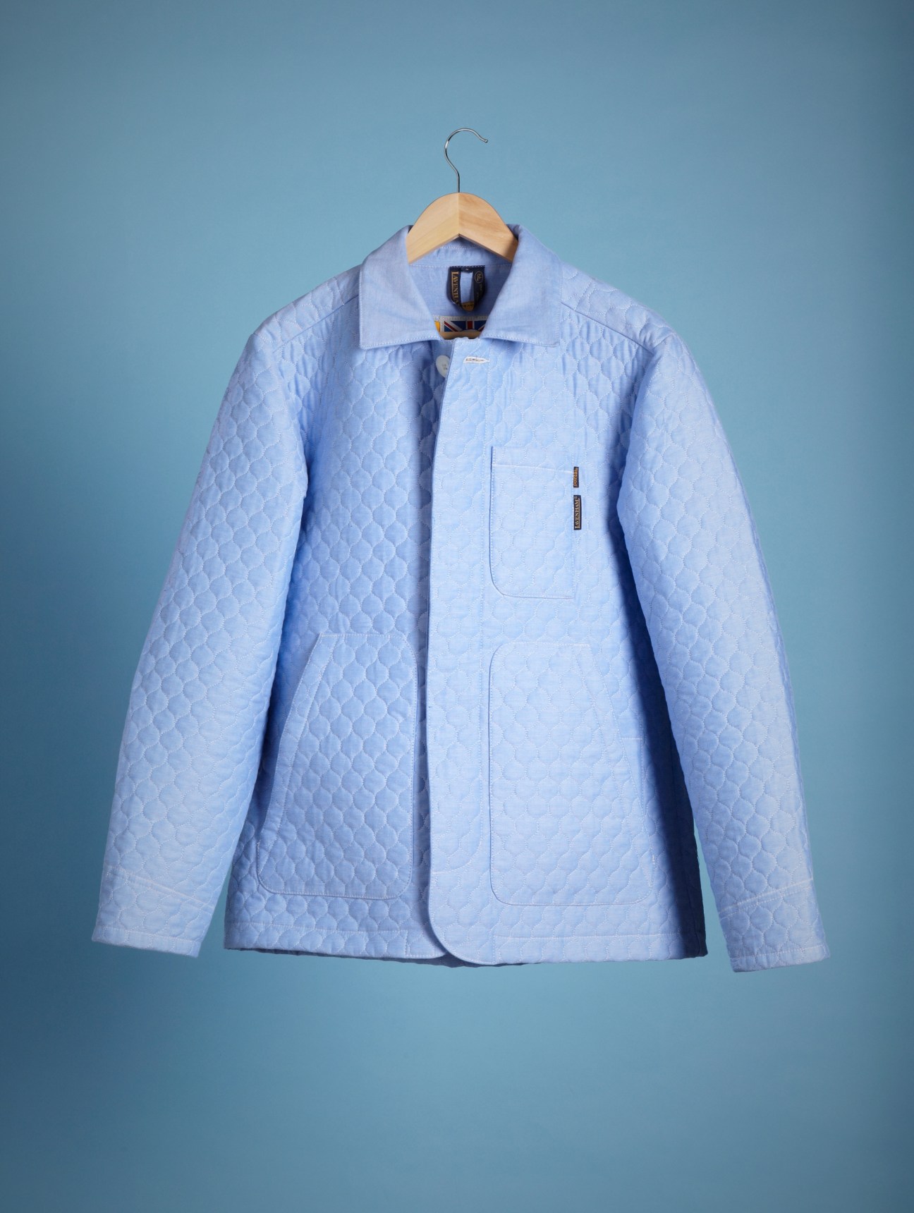 Light blue quilted jacket on wooden hanger against blue background.