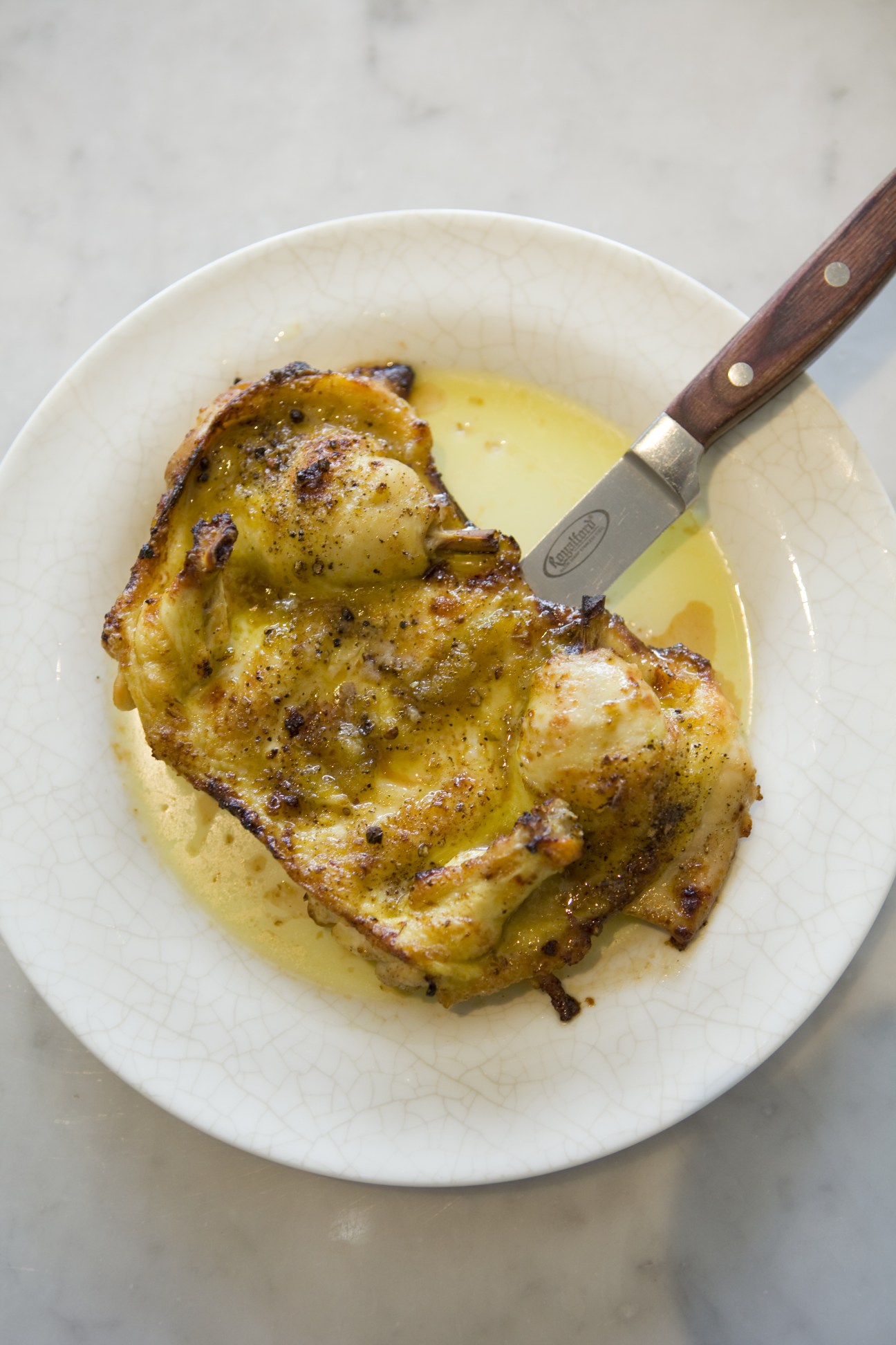 Roast baby chicken marinated in lemon served on a white plate with butter sauce and a knife.