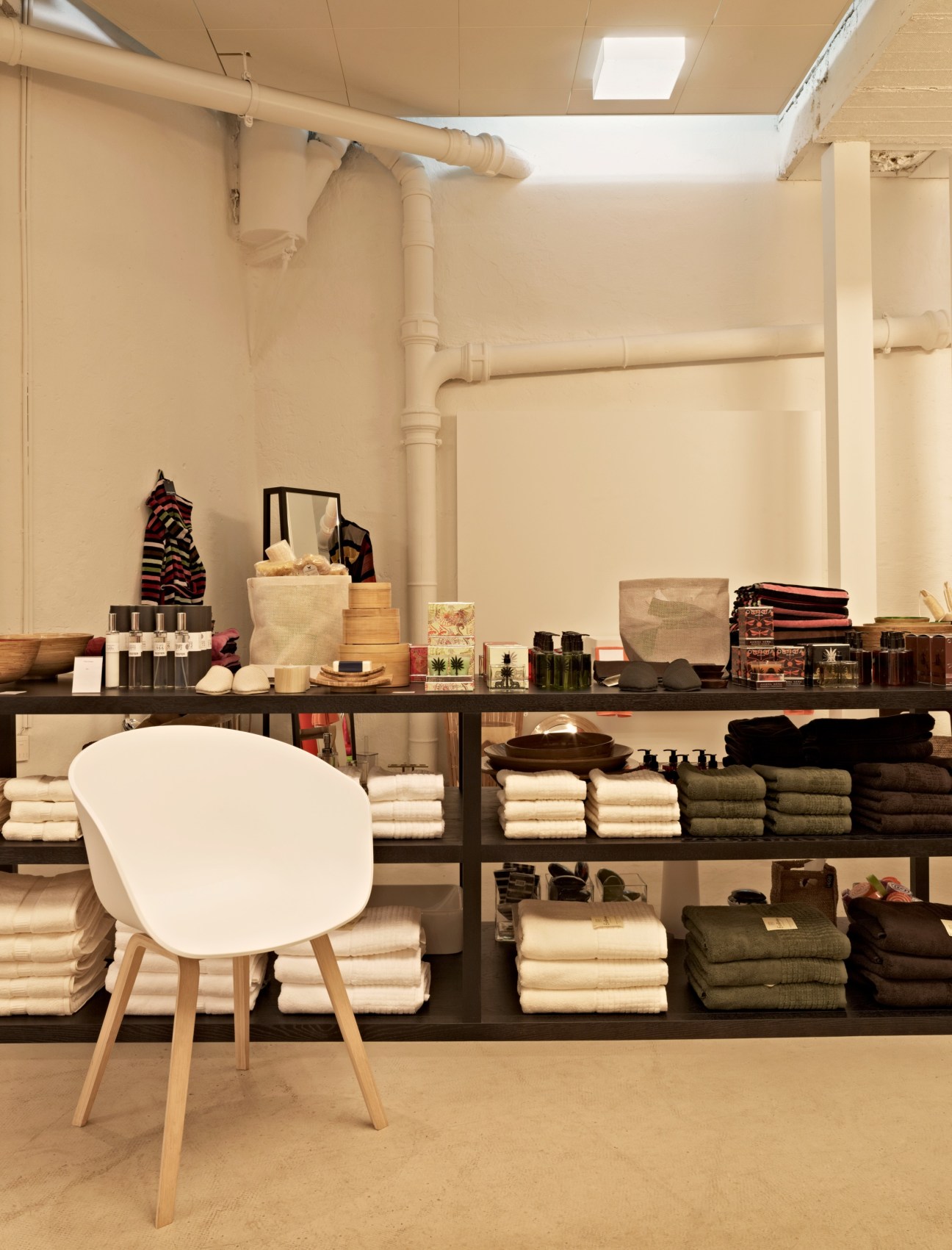 White modern chair by Hay displayed in Badrummet bathroom boutique with shelves of towels and beauty products.