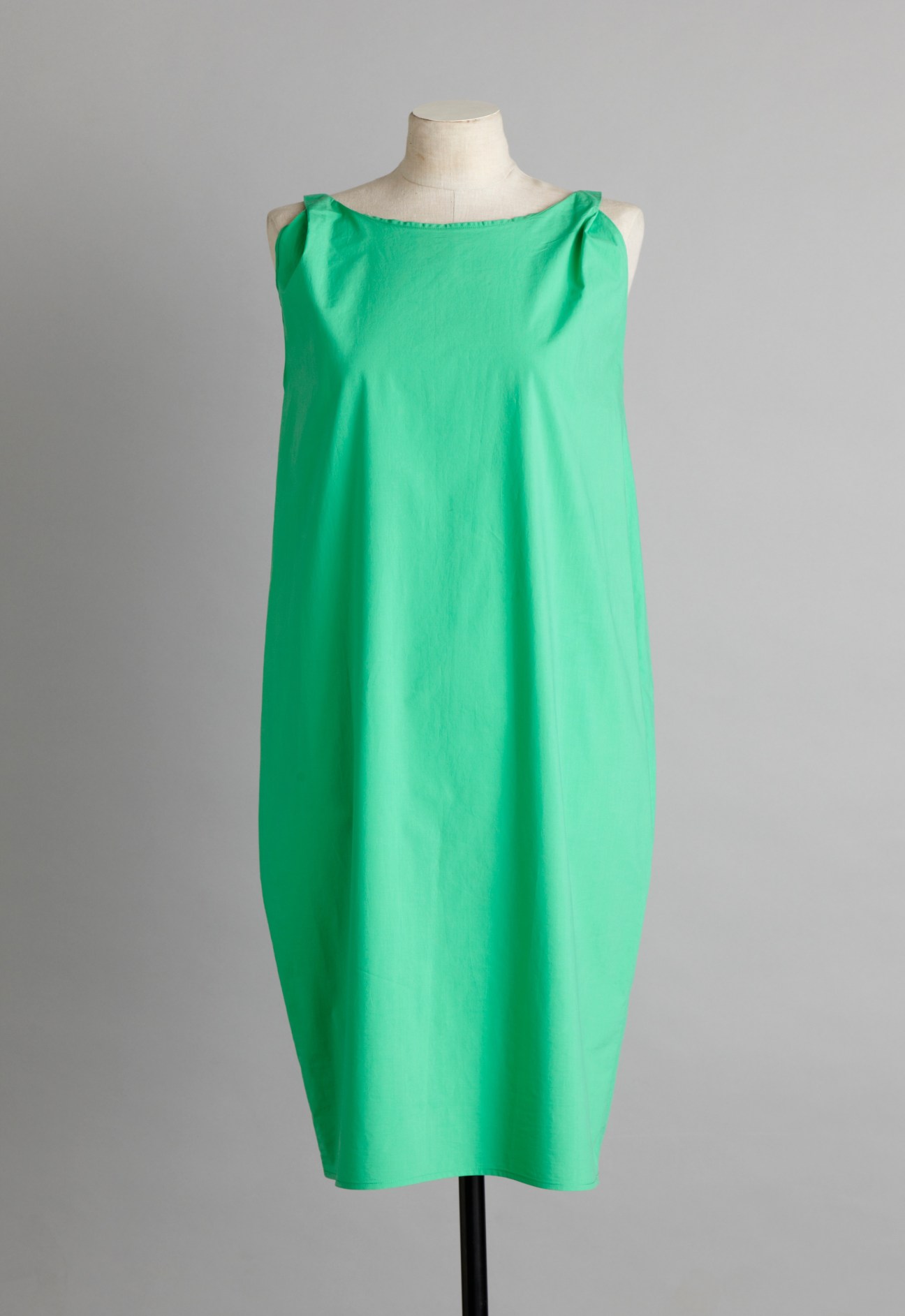 Green cotton poplin sleeveless dress on a dress form with geometric neckline and structured silhouette.
