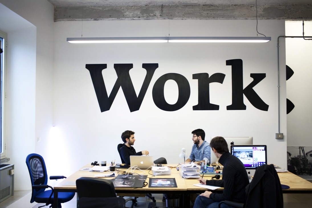 Team working at a table in Superegg advertising agency office with "WORK" text on wall.