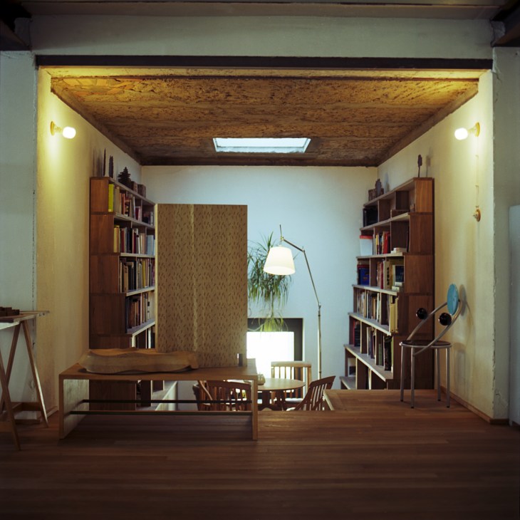 A modern reading room with wooden shelving, cork ceiling, desk, and arc floor lamp.