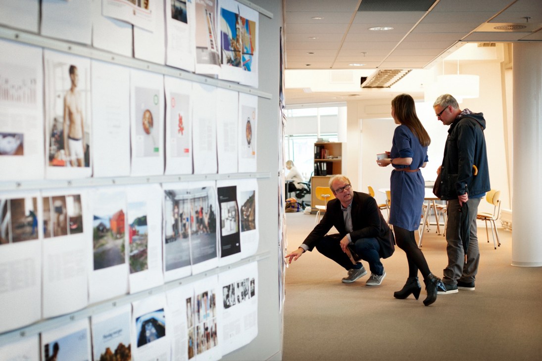 Staff members viewing layout pages and designs on a wall in the Dagens Næringsliv newsroom.