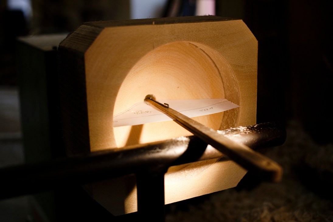 Wooden mould with glowing interior and measuring tool for glass piece production.