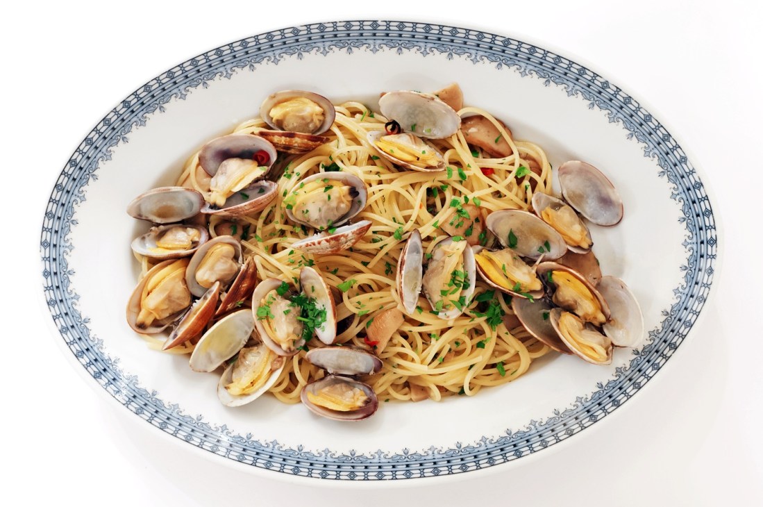Porcini and clam pasta served on a white plate with blue decorative border.