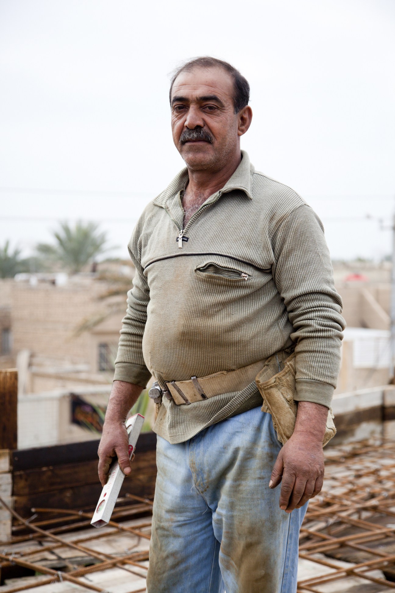 Construction site foreman Emad Najar stands on a Baghdad building site with palm trees in background.