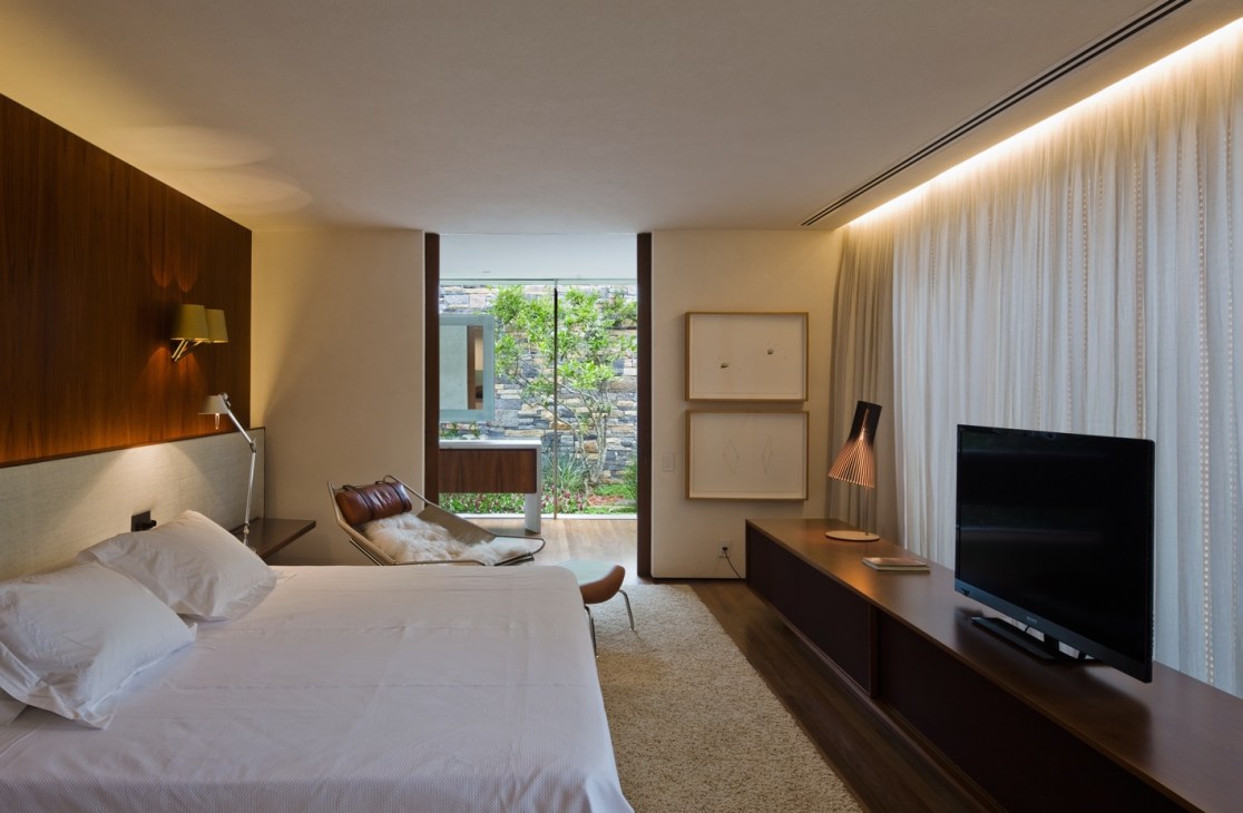 Master bedroom with white bed, wood furnishings, glass doors opening to garden view, and minimal decor.