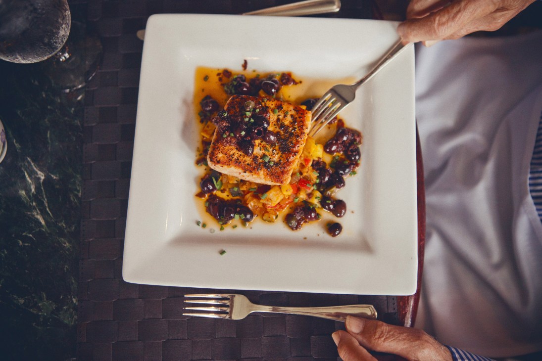Pan roasted king salmon with ratatouille, black olives and capers on a white square plate.