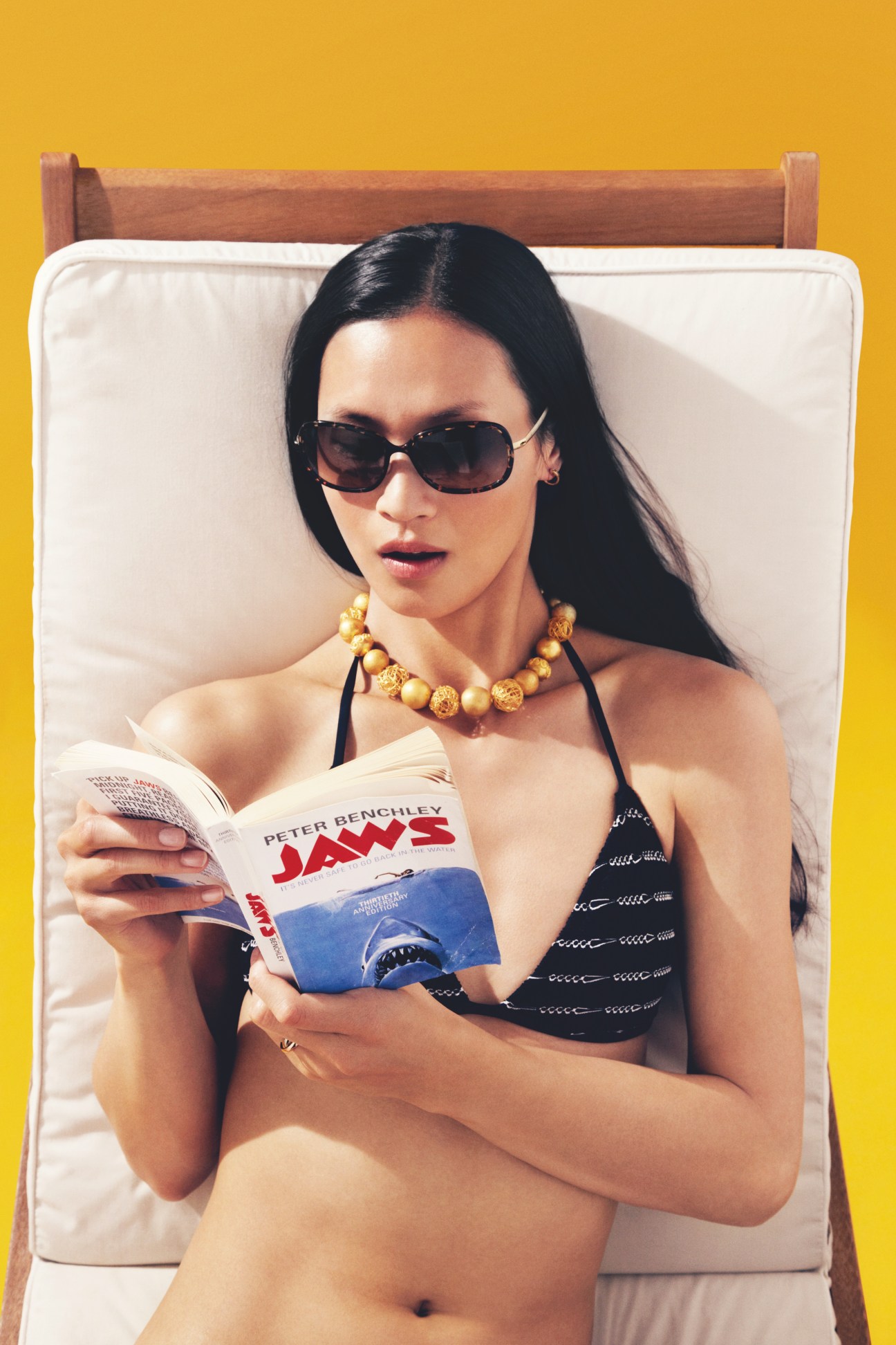 Model on lounger wearing Lindberg sunglasses, Cartier earrings, Firouzeh necklace, Polo Ralph Lauren bikini and Louis Vuitton ring, reading a book