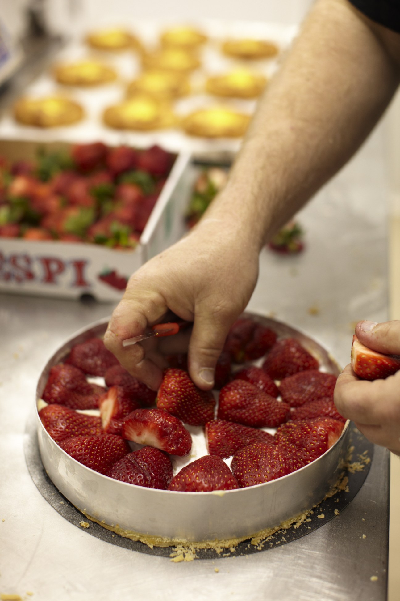 A hand placing a strawberry on a cake topped with fresh strawberries at Fibonacci bakery.