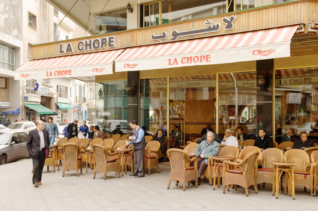 Café La Chope storefront in Casablanca with red and white striped awning and wicker chairs on the street.