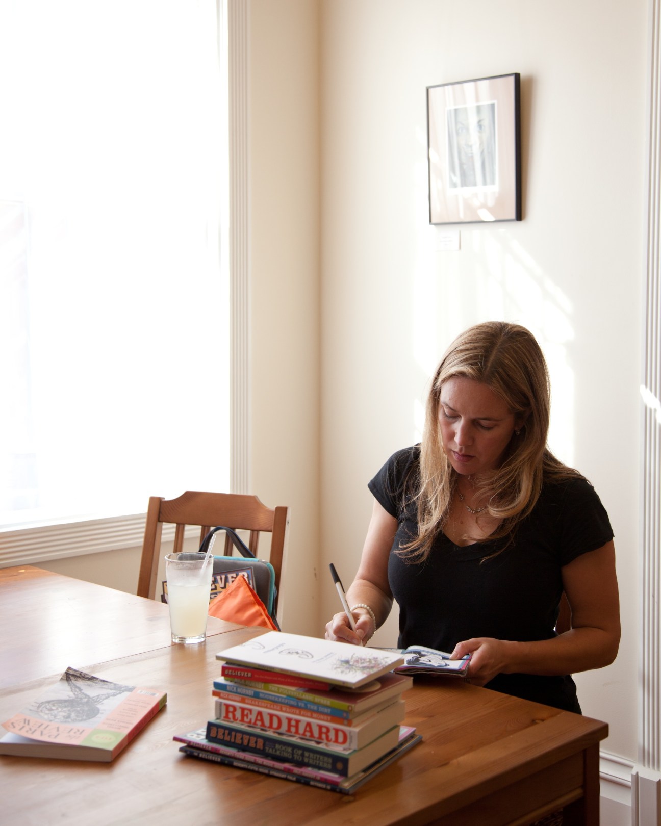 Vendela Vida writing at a wooden desk in a bright, minimalist office space with a stack of books.