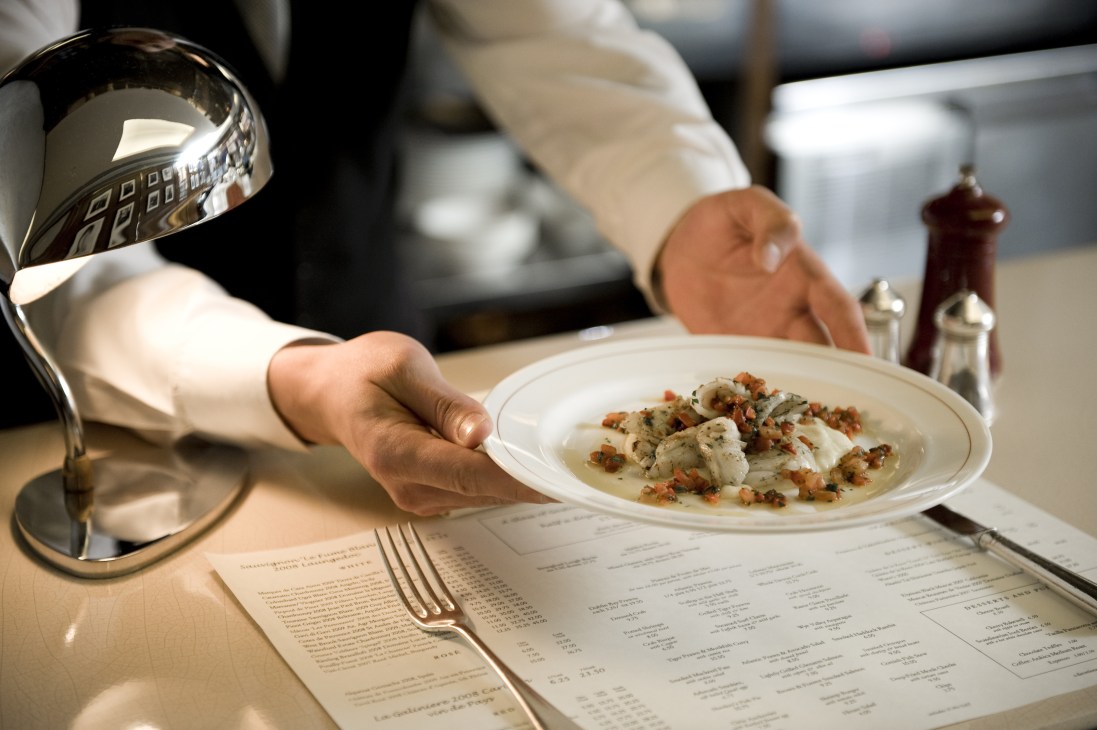 A plate of chargrilled cuttlefish with soft polenta and red pepper being served at a restaurant table.