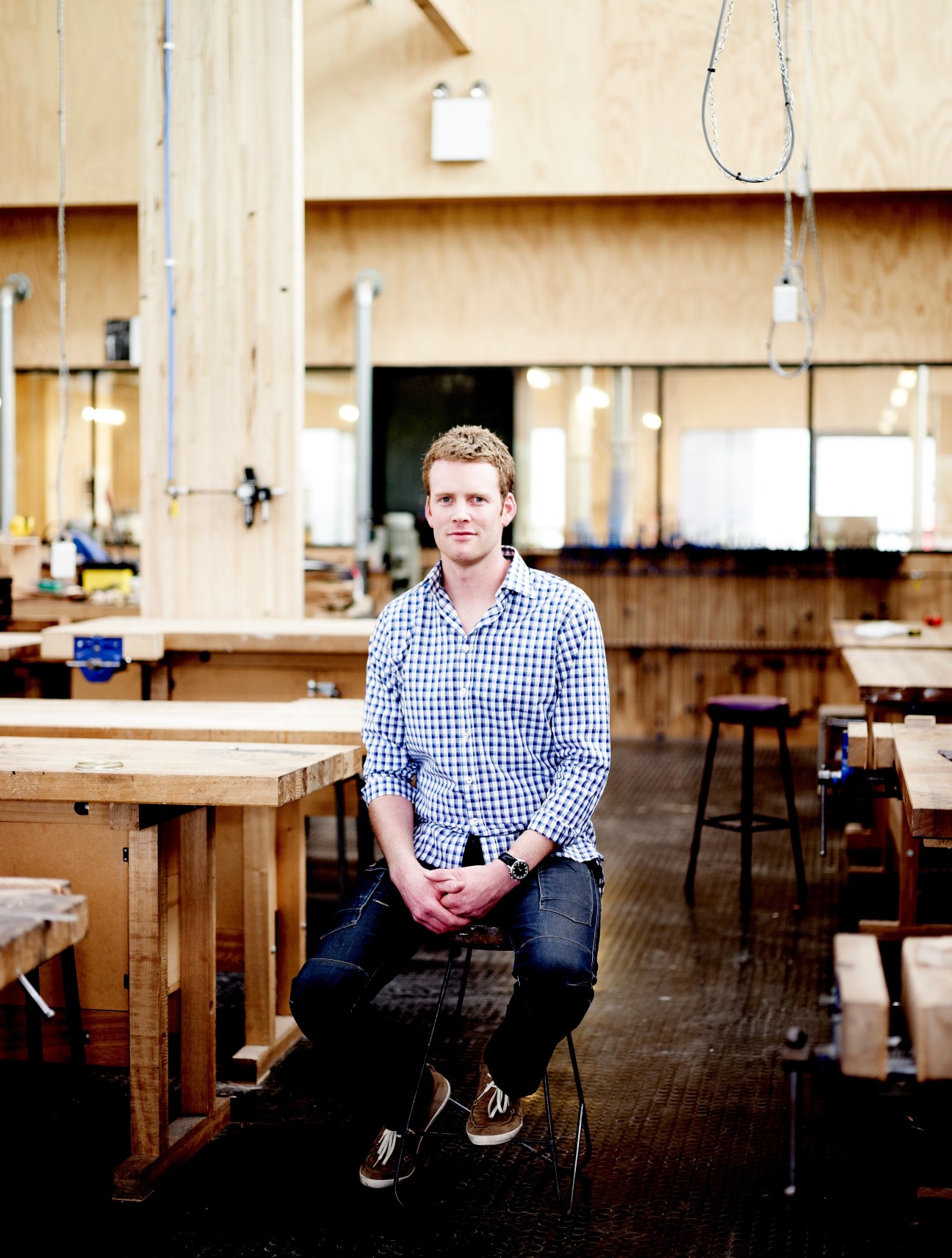 Simon Ancher sits in a woodworking workshop with workbenches and tools visible.
