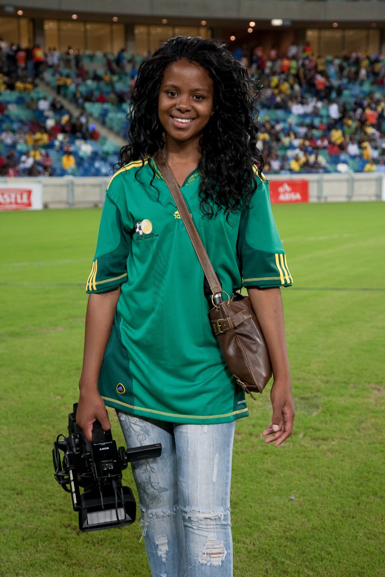 Young female camerawoman holding professional video camera on stadium field during World Cup match.