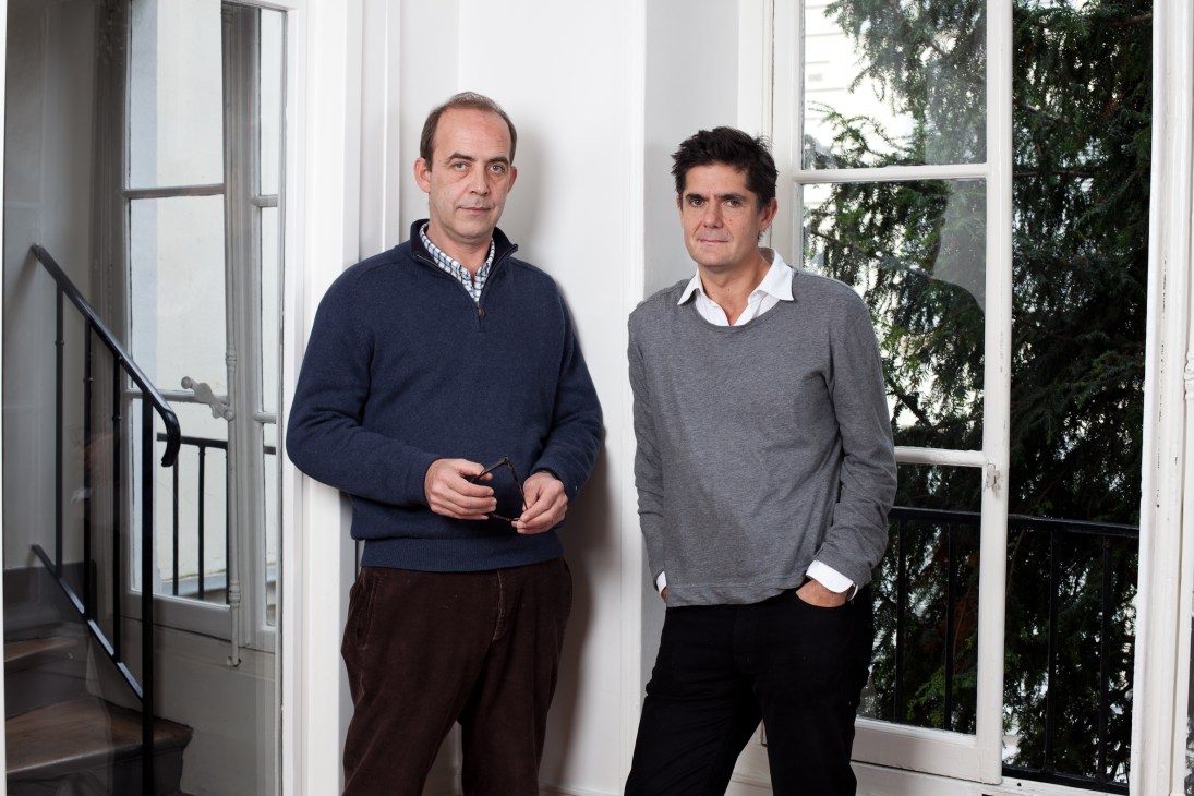 Patrick de Saint-Exupéry and Laurent Beccaria, founders of XXI magazine, standing in an office with large windows.