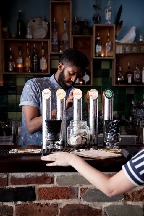Bartender pouring a drink at The Bird bar with multiple beer taps and shelves of bottles behind the counter.