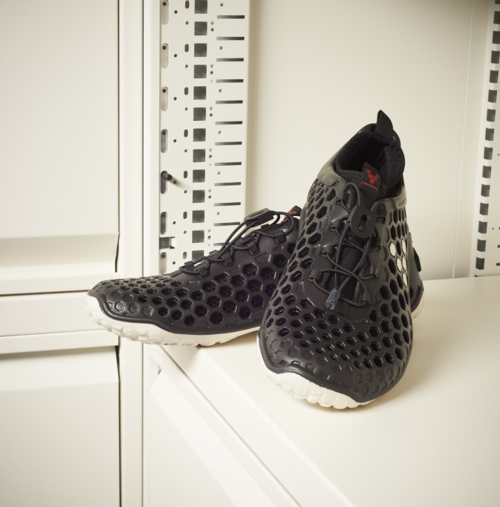 Pair of black Vivobarefoot running shoes with white sole displayed on white shelf.
