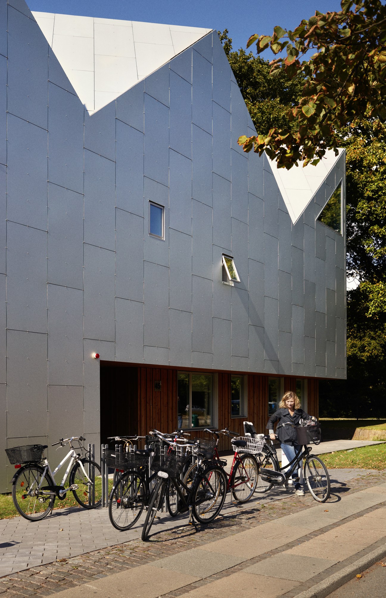 Center for Cancer and Health building exterior with aluminium facade and pitched roof, showing main entrance and bicycle parking.