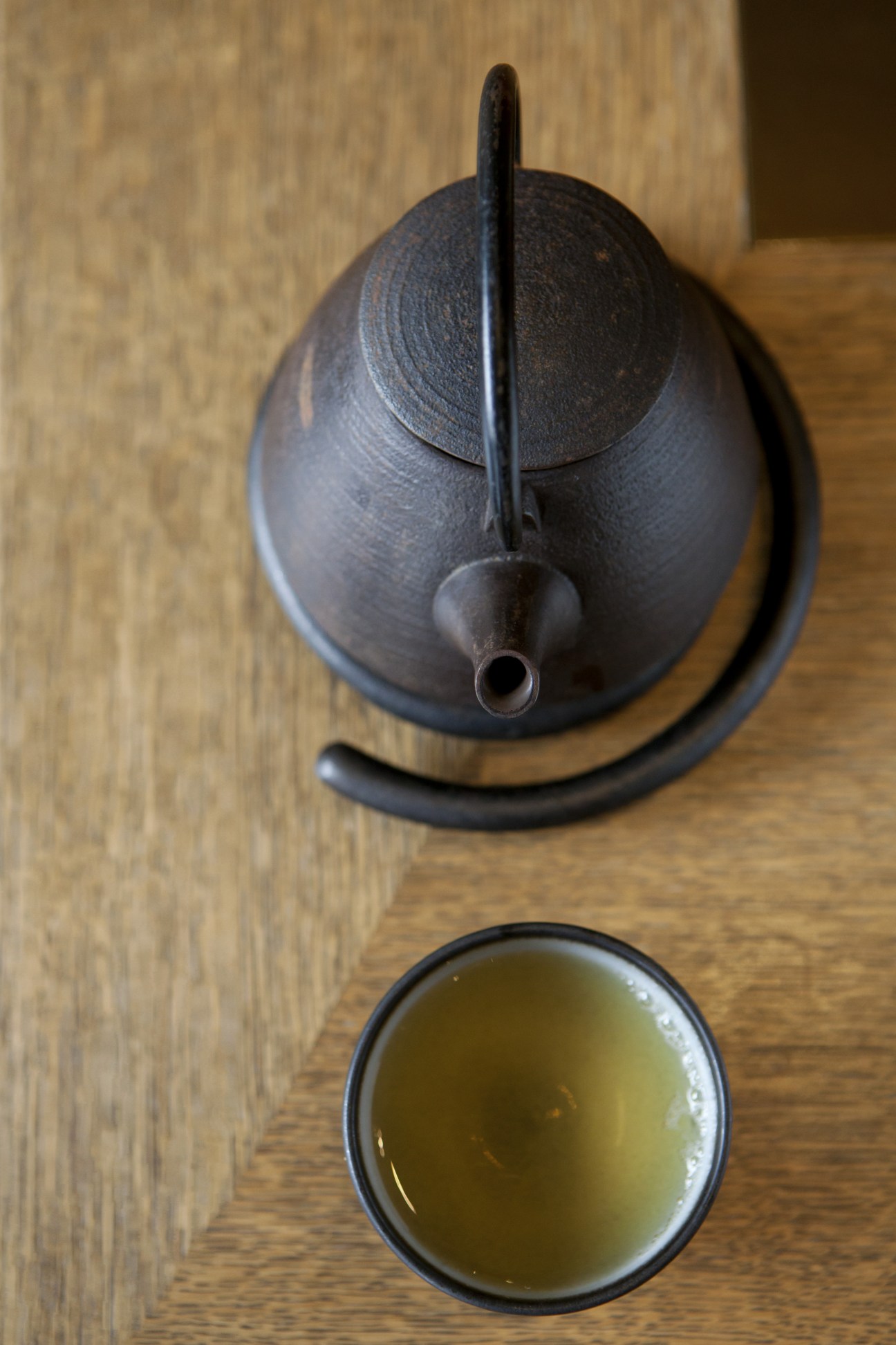 Japanese green tea in a black cup next to a dark cast iron teapot.