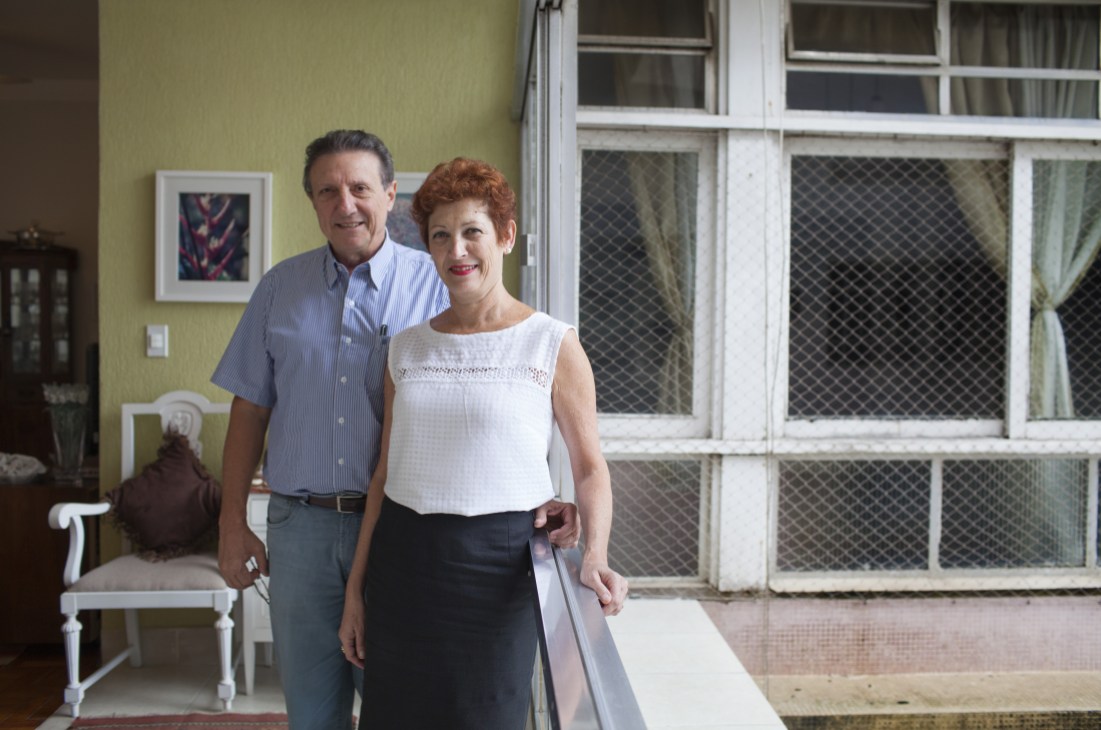 Marcos Prandi and Sonia Kapulski stand in their apartment with yellow walls and large windows overlooking the beach.