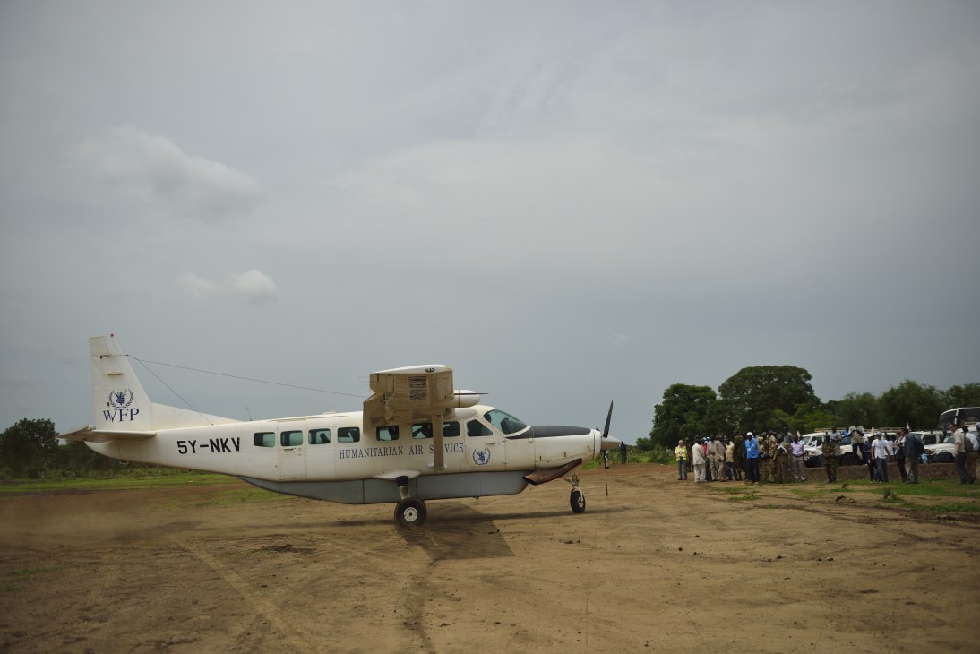 WFP humanitarian aircraft on dusty airstrip with people gathered nearby in South Sudan.