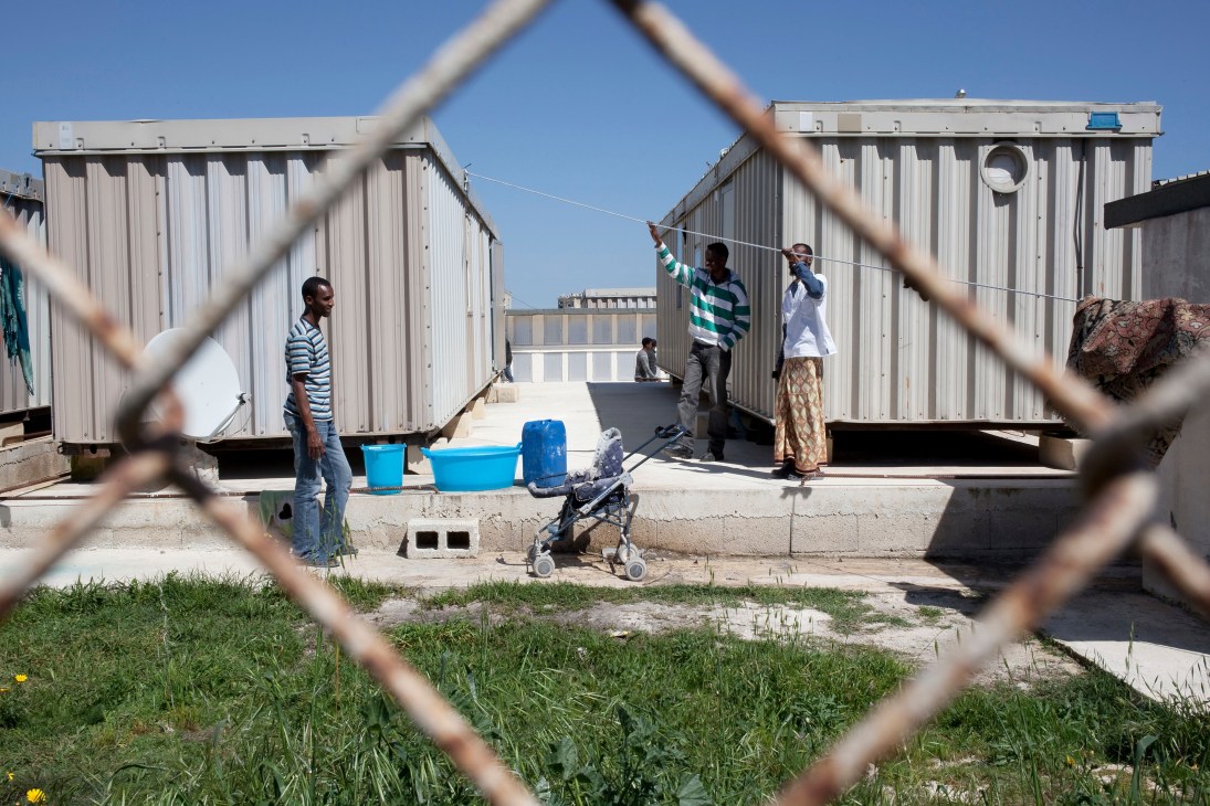 Migrants and asylum seekers at a shelter with corrugated metal structures at Hal Far in Malta.