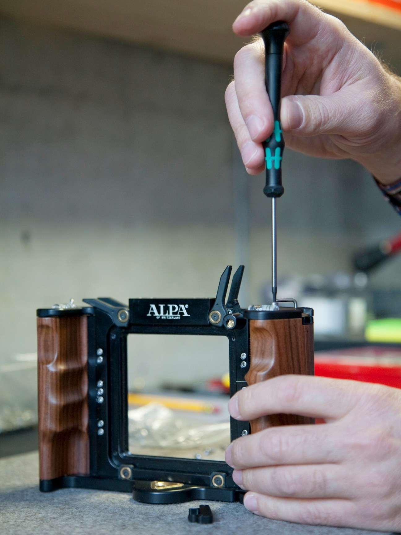 Hands assembling an Alpa camera body with rosewood handgrip and precision adjustment mechanism.