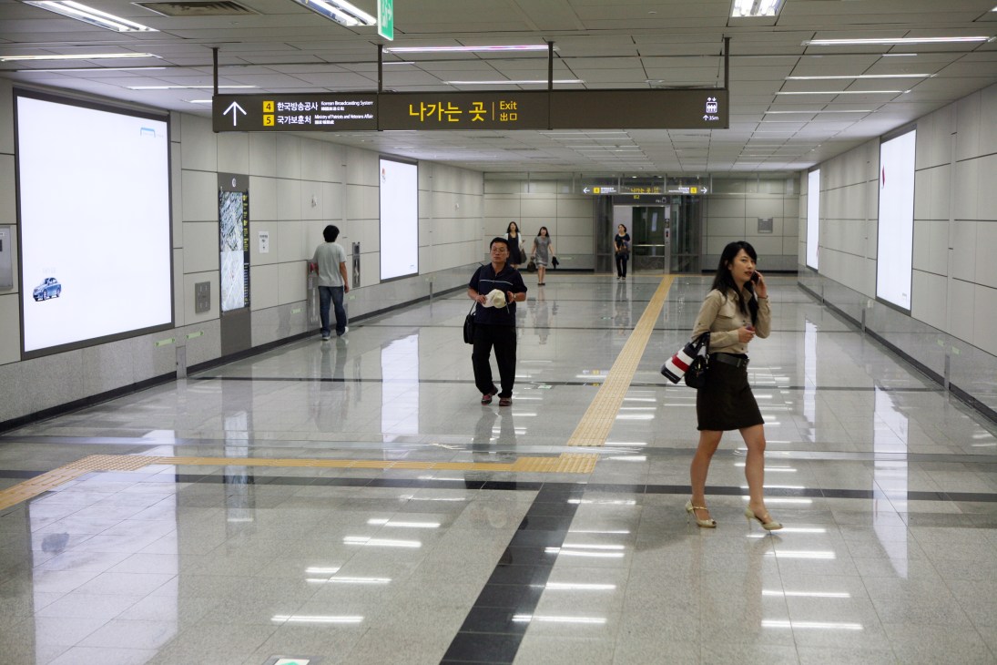 Seoul subway station corridor with minimalist white Hyundai Card advertisement hoardings on walls and commuters walking.