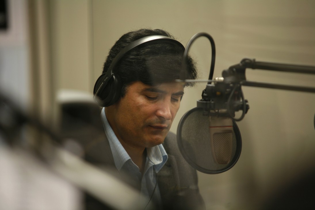 Broadcaster Asmat Sarwan wearing headphones speaks into a studio microphone.