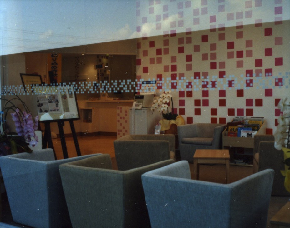 Sugamo Shinkin Bank Niiza branch interior with colorful red and white square pattern wall, seating area with gray chairs, and modern design elements.