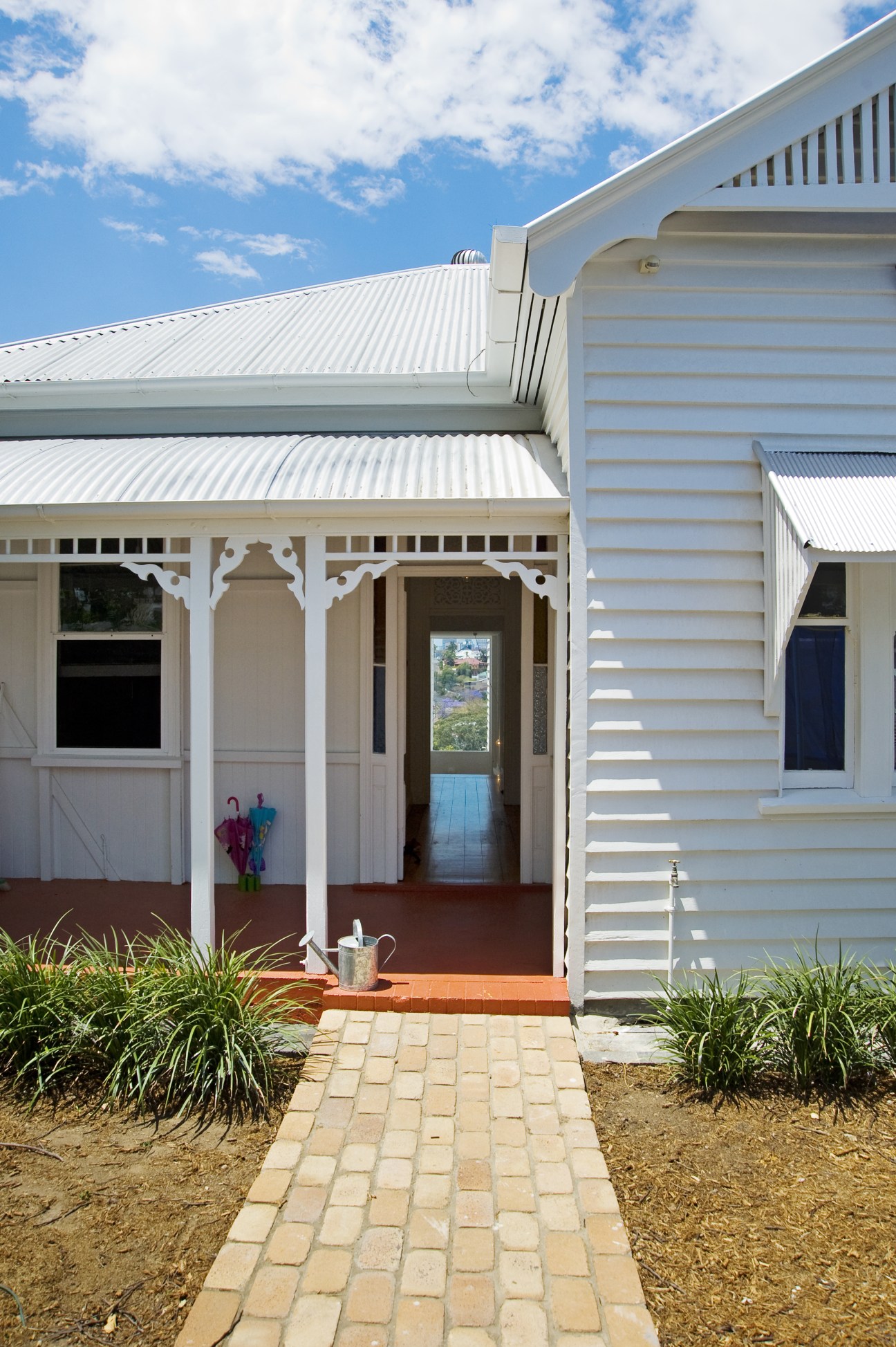 White weatherboard cottage with traditional porch featuring decorative brackets and ornamental details under a corrugated metal roof.