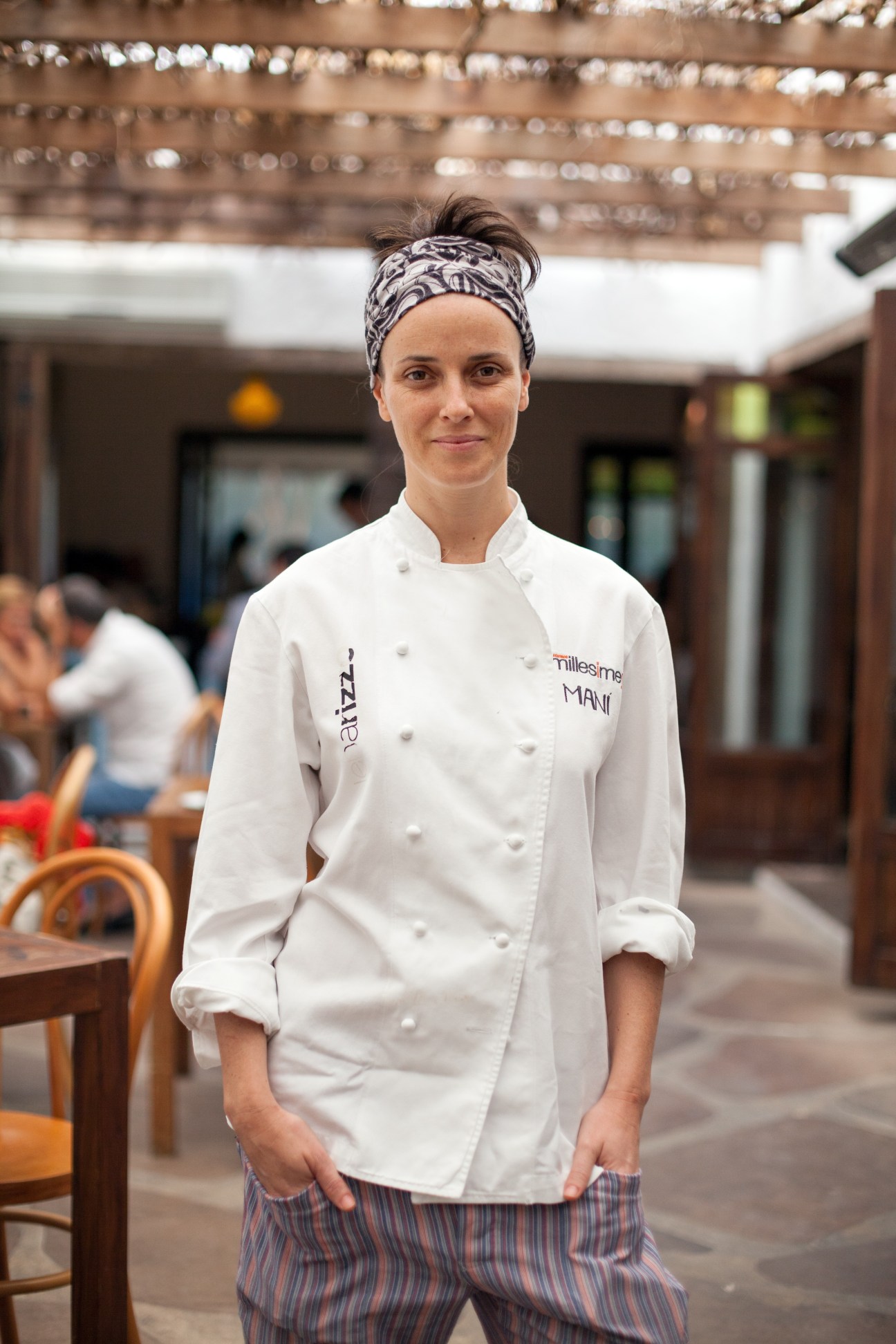 Chef in white double-breasted jacket with headband standing in restaurant courtyard at Maní.